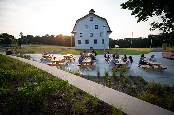 Photo of several people gathering at picnic tables on Chatham University's 伊甸堂校园 in front of a white barn. 